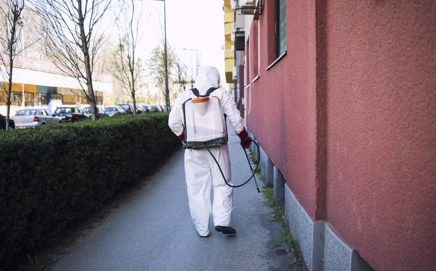 Unrecognizable worker in chemical protection suit spraying disinfectant on public surfaces. Property Protection Services